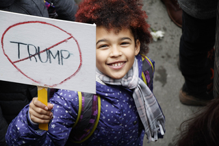 A child in the New York City sister march holds a small sign with Trump's name crossed out.